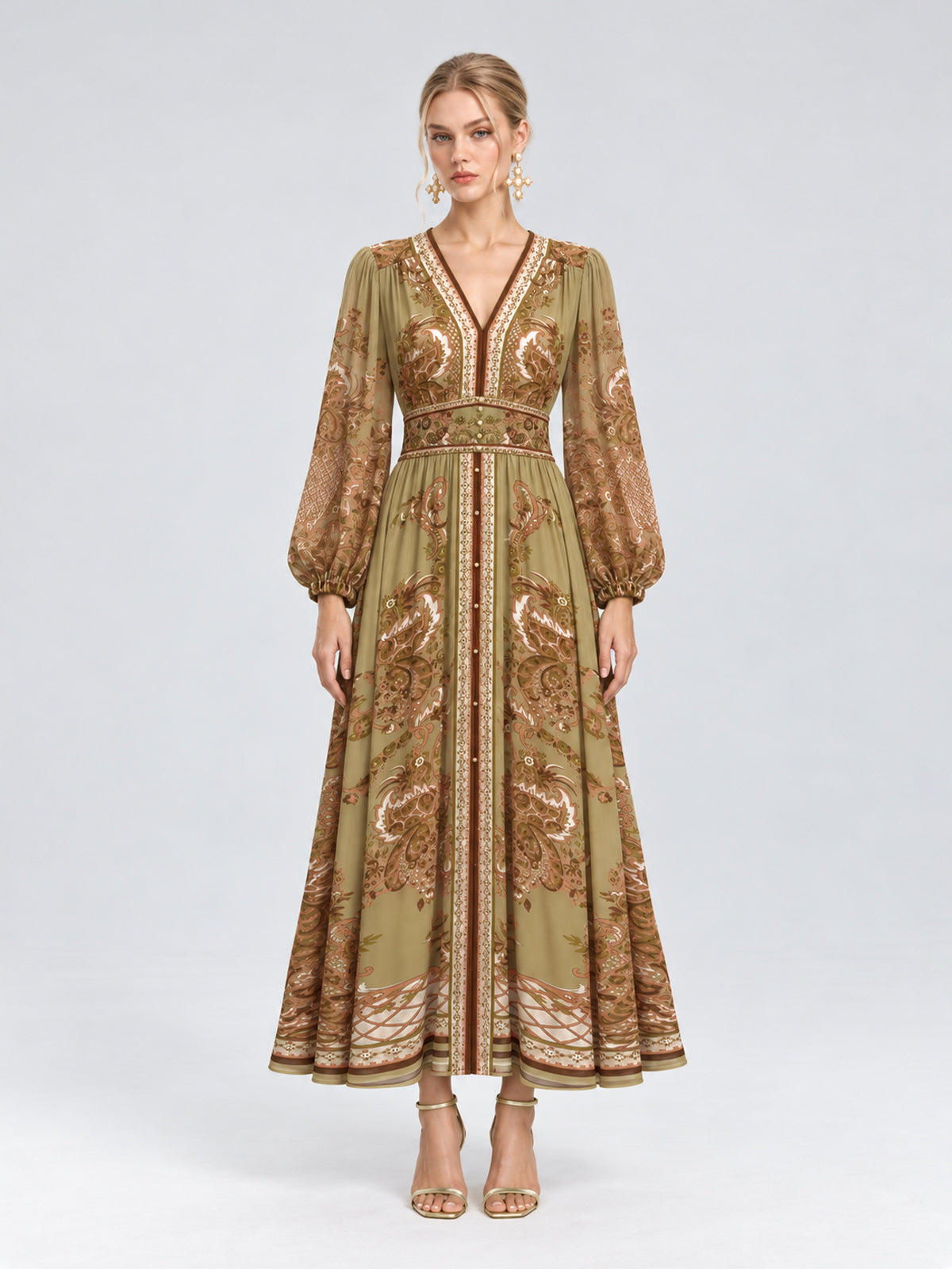 A woman wearing the Social Queen Paisley Print Mulberry Silk Dress, featuring a long, olive green and brown paisley floral pattern with long sleeves and a v-neck, stands against a plain light background. With a neutral expression and open-toed heels, she showcases this effortlessly elegant resort wear piece that combines both comfort and style.