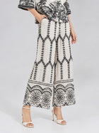 A person wearing the Social Queen Geometric Print Pleated Wide-Leg Pants with a matching top and white heeled sandals, standing with hands in pockets against a plain background.
