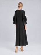 A woman stands with her back to the camera wearing the Social Queen 3D Floral Pleated Dress, a long black maxi design featuring ruffled sleeves, paired with gold earrings and gold heels.