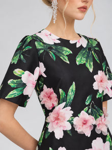 A woman wearing the Social Queen 3D Peony Floral Shift Dress, featuring a black background with pink peony floral print and short sleeves, accessorized with dangling rhinestone earrings.