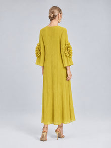 A woman stands facing away, wearing the Social Queen 3D Floral Pleated Dress, featuring pleated fabric and floral appliqué accents on the sleeves, paired with gold high heels.