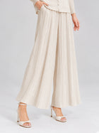 A model showcases the 3D Floral Pleated Two-Piece Set by Social Queen, featuring pleated wide-leg beige trousers and white high-heeled sandals, standing against a plain background. The ensemble captures effortless elegance, with the pleated design adding soft movement to the look.