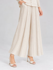 A model showcases the 3D Floral Pleated Two-Piece Set by Social Queen, featuring pleated wide-leg beige trousers and white high-heeled sandals, standing against a plain background. The ensemble captures effortless elegance, with the pleated design adding soft movement to the look.