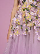 Close-up of a person in the Social Queen 3D Daisy Embroidered Tulle Dress, a lavender A-line style with yellow, white, and green daisy embroidery, set against a pink background.