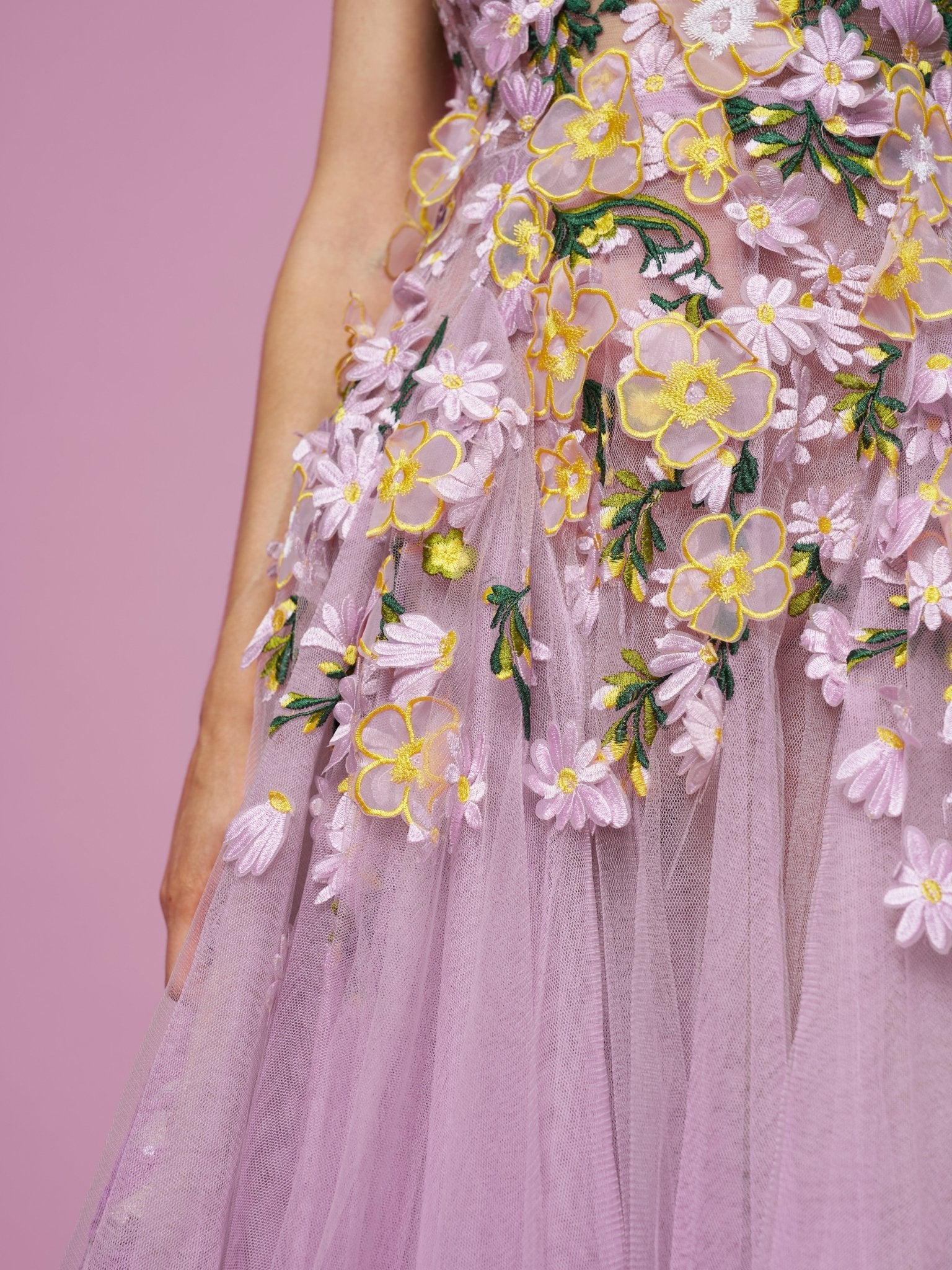 Close-up of a person in the Social Queen 3D Daisy Embroidered Tulle Dress, a lavender A-line style with yellow, white, and green daisy embroidery, set against a pink background.