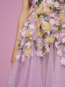 Close-up of a person in the Social Queen 3D Daisy Embroidered Tulle Dress, a lavender A-line style with yellow, white, and green daisy embroidery, set against a pink background.