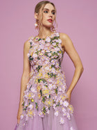 A woman stands against a pink background wearing the Social Queen 3D Daisy Embroidered Tulle Dress, a sleeveless lilac A-line adorned with yellow and white floral appliqués.