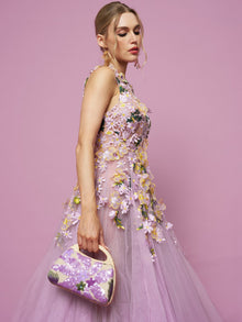 Woman in the Social Queen 3D Daisy Embroidered Tulle Dress, featuring a lavender floral A-line silhouette, holds a purple handbag against a solid pink background.