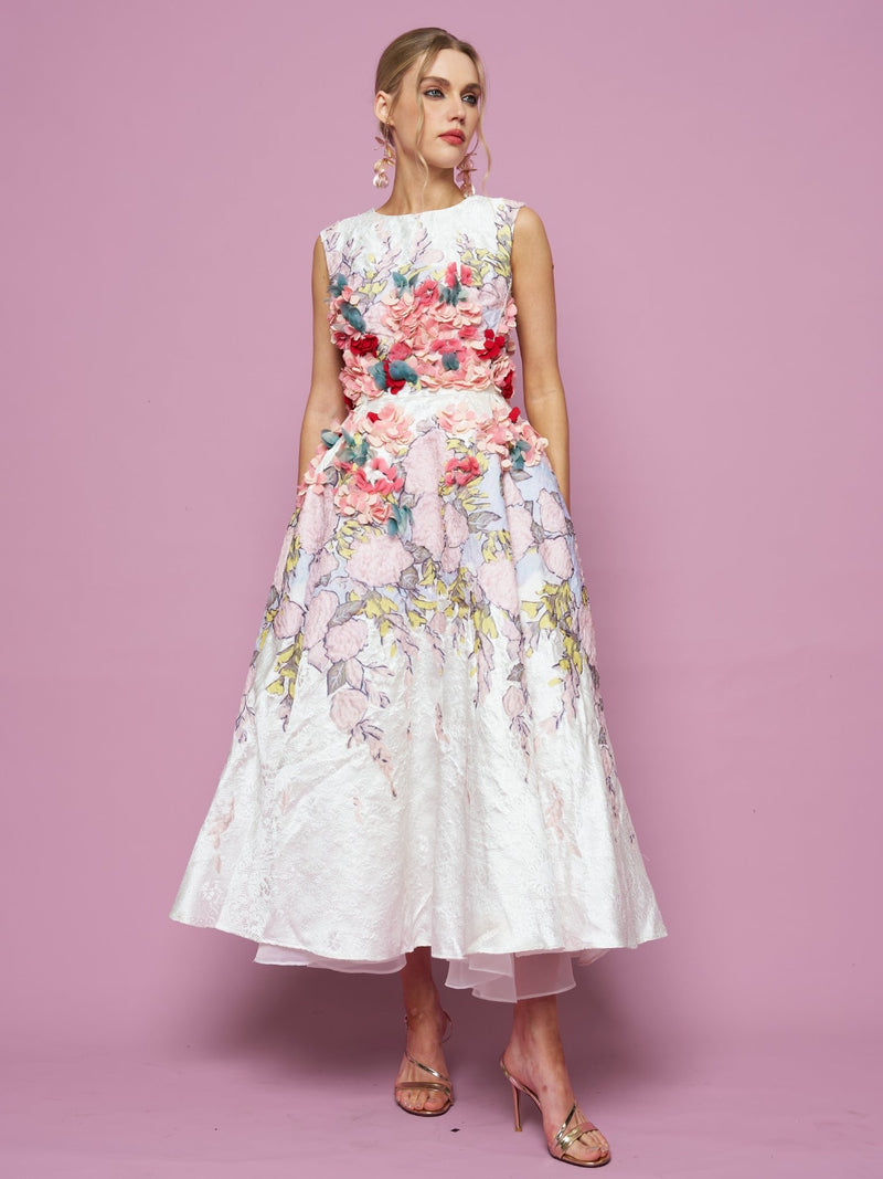 A woman in the Social Queen 3D Floral Embellished Jacquard Gown with a flared skirt and pink heels stands against a pink background.