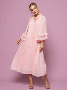 A woman models the Social Queen 3D Floral Embellished Silk Dress, featuring light pink mulberry silk, pleats, long sleeves, and floral neckline accents, set against a solid pink background.