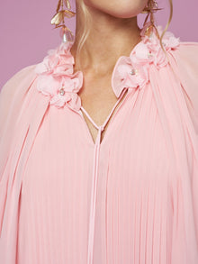 Close-up of a person wearing Social Queen's 3D Floral Embellished Silk Dress in light pink, featuring pleats and 3D floral details on the shoulders, styled with gold leaf earrings against a pink backdrop.