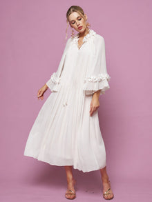 A woman wears the Social Queen 3D Floral Embellished Silk Dress—flowing pale pink mulberry silk with pleats and 3D floral details on the collar and sleeves—set against a solid pink background.