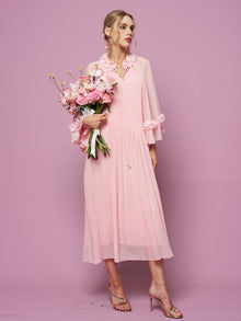 Woman in a light pink Social Queen 3D Floral Embellished Silk Dress with long sleeves and 3D floral appliqué, holding a bouquet of pink flowers against a pink background, styled with heeled sandals.