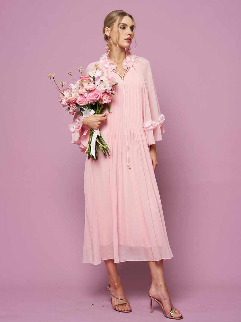 Woman in a light pink Social Queen 3D Floral Embellished Silk Dress with long sleeves and 3D floral appliqué, holding a bouquet of pink flowers against a pink background, styled with heeled sandals.