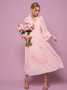 A woman wears Social Queen’s 3D Floral Embellished Silk Dress, light pink and adorned with floral appliqué, as she holds a bouquet of pink and white flowers against a pink background.