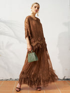 A woman stands against a white wall, wearing the Social Queen 3D Floral Embroidered 100% Silk Ruffle Blouse with black sandals and holding a small green handbag.