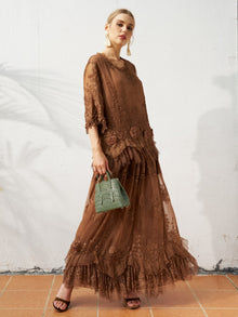 A woman stands against a white wall, wearing the Social Queen 3D Floral Embroidered 100% Silk Ruffle Blouse with black sandals and holding a small green handbag.