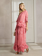 A woman stands indoors wearing the Social Queen 3D Floral Embroidered 100% Silk Ruffle Blouse, paired with a small purse and heeled sandals.