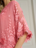 Close-up of a person in the Social Queen 3D Floral Embroidered 100% Silk Ruffle Blouse, featuring pink sheer fabric, lace details, and appliqué flowers on the sleeves and bodice.