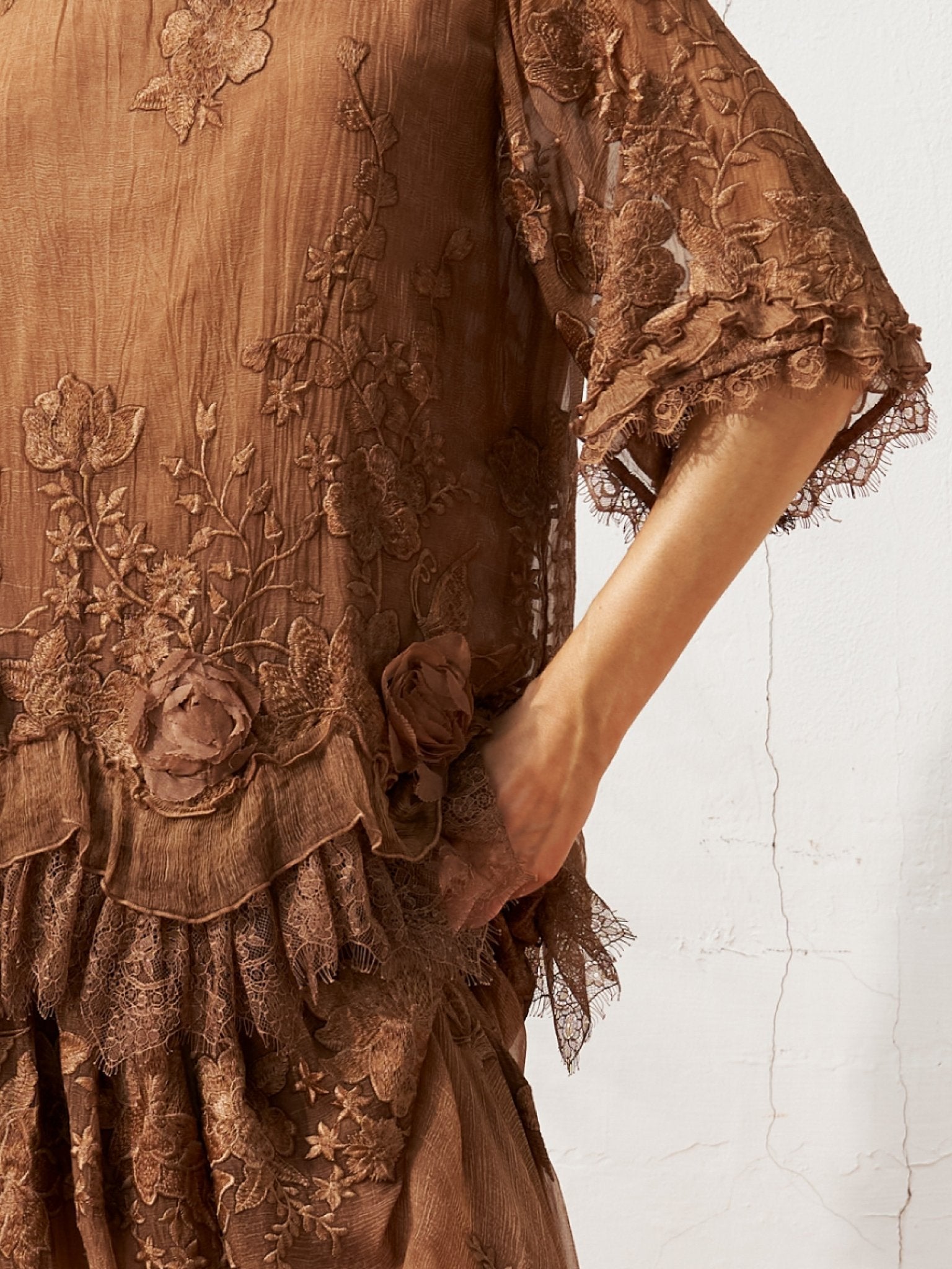A person wears the Social Queen 3D Floral Embroidered 100% Silk Ruffle Blouse, standing against a textured white wall with one hand resting in a side pocket.
