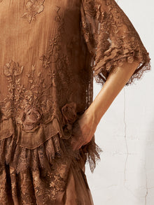 A person wears the Social Queen 3D Floral Embroidered 100% Silk Ruffle Blouse, standing against a textured white wall with one hand resting in a side pocket.