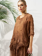 Indoors, a woman wears the Social Queen 3D Floral Embroidered 100% Silk Ruffle Blouse, paired with large earrings and a green-handled bag. A palm leaf appears in the background.