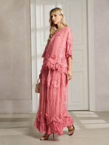 Indoors, a woman wears the Social Queen 3D Floral Embroidered 100% Silk Ruffle Skirt with high-heeled sandals, earrings, and a small handbag.