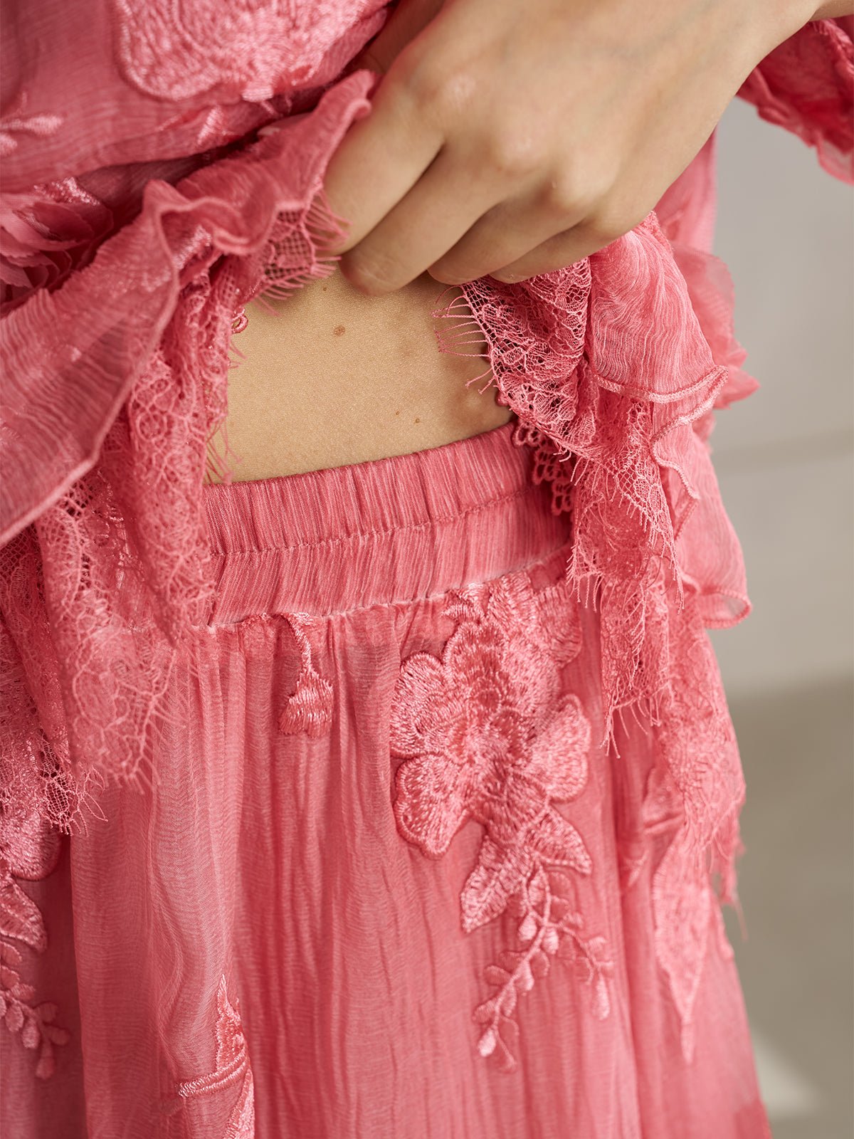 A person lifts the hem of a Social Queen 3D Floral Embroidered 100% Silk Ruffle Skirt, revealing part of their midriff.