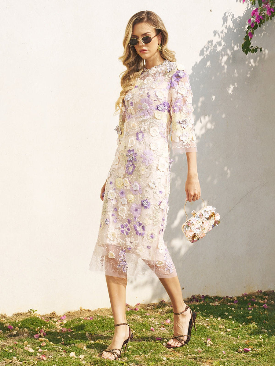 Woman in a Social Queen 3D Floral Embroidered Beaded Dress and sunglasses, carrying a matching handbag, strolls on grass by a white wall—a chic pick for wedding guests.