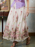 A person wearing Social Queen’s 3D Floral Embroidered Silk Skirt and gold heels stands indoors beside a wooden table and a framed painting.