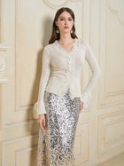 Indoors, a woman wears the Social Queen 3D Floral Lace Wool-Silk Knit Top with ruffled lace cuffs and a long silver sequin skirt, accessorized with drop earrings.