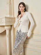 A woman wearing the Social Queen 3D Floral Lace Wool-Silk Knit Top and a silver sequin skirt stands indoors beside a cream-colored fireplace, looking at the camera.