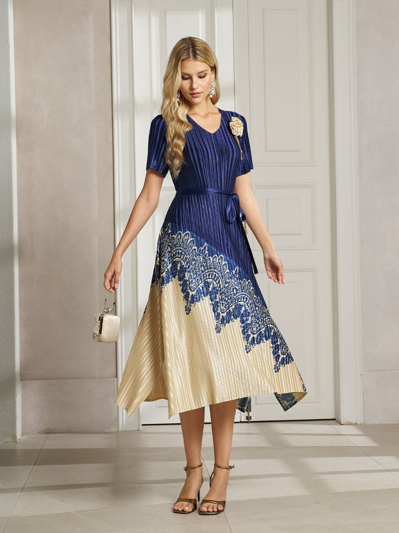 A woman wearing the Social Queen 3D Floral Plissé Satin Lace-Print Dress stands indoors, holding a small handbag and looking down, with one leg slightly forward.