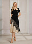 A woman stands indoors in front of white paneled doors, wearing the Social Queen 3D Floral Plissé Satin Lace-Print Dress with a belted waist and gold sandals.