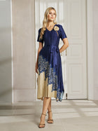 A woman poses indoors in front of white paneled doors, wearing the Social Queen 3D Floral Plissé Satin Lace-Print Dress with navy blue and beige tones, short sleeves, floral details, and strappy heels.