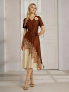 A woman stands indoors wearing the Social Queen 3D Floral Plissé Satin Lace-Print Dress, a brown and beige short-sleeve midi dress with a belted waist and heeled sandals.