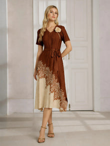 A woman stands indoors wearing the Social Queen 3D Floral Plissé Satin Lace-Print Dress, a brown and beige short-sleeve midi dress with a belted waist and heeled sandals.