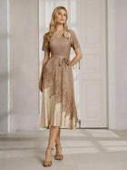 A woman stands indoors wearing the Social Queen 3D Floral Plissé Satin Lace-Print Dress, featuring short sleeves, a tie waist, pleated bodice, knee length, and intricate lace-print accents.