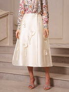 A person stands on marble steps indoors wearing a floral long-sleeve blouse, strappy heels, and the Social Queen 3D Floral Satin Midi Skirt—perfect for wedding guests.