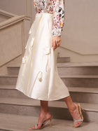 A woman stands on stairs in the Social Queen 3D Floral Satin Midi Skirt, styled with a floral long-sleeve blouse and heels—a chic wedding guest skirt choice for special occasions.