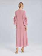 A woman stands with her back to the camera, wearing the Social Queen 3D Floral Pleated Dress—a pink, long-sleeve maxi dress featuring pleats and delicate 3D floral appliqué embellishments on the sleeves—paired with gold high heels.