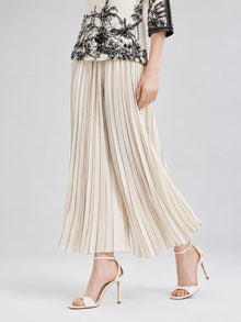 A woman models the Social Queen Striped Pleated Wide-Leg Pants with a black and white patterned top and cream high-heeled sandals, set against a neutral backdrop.