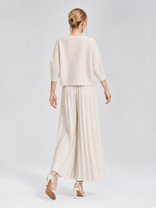 A person stands on a white background, facing away, wearing the Social Queen 3D Floral Pleated Two-Piece Set—featuring a cream-white loose top and pleated wide-leg trousers—paired with high-heeled shoes.