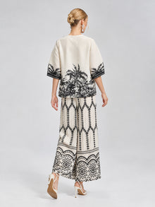 A woman stands with her back to the camera, wearing Social Queen’s Geometric Print Pleated Wide-Leg Pants in cream with a black geometric pattern, paired with white high-heeled sandals against a plain background.