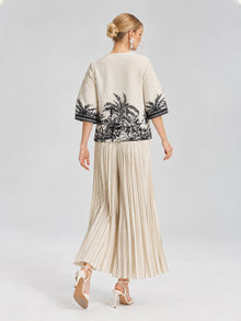 A woman, seen from behind in a cropped silhouette as she walks against a light gray background, wears the Social Queen Palm Tree Print Pleated Blouse paired with a cream skirt.