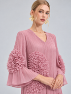 A woman poses against a plain light gray background wearing the Social Queen 3D Floral Pleated Dress, a pink maxi dress featuring pleats and large ruffled floral appliqué accents on the sleeves and waist, styled with gold flower-shaped earrings.