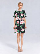 A woman stands against a light grey background wearing the Social Queen 3D Peony Floral Shift Dress, a short-sleeved, knee-length black shift dress adorned with soft pink peony flowers and green leaves, paired with open-toe heels.