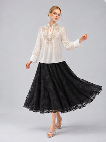 A woman models the Social Queen Floral Vine Embroidered Blouse in ivory, paired with a long black lace skirt featuring a relaxed straight silhouette, standing against a plain gray background.