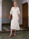 A woman stands indoors on a tiled floor in front of a wooden door, wearing the Social Queen Geometric Jacquard Mulberry Silk Dress with heels and holding a colorful woven bag.