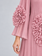 A person, shown from the neck down, wears the Social Queen 3D Floral Pleated Dress—a pleated pink maxi dress featuring large ruffled floral appliqué embellishments on the sleeve and side.